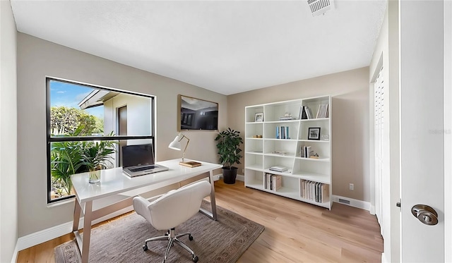 office area with baseboards, light wood finished floors, and visible vents