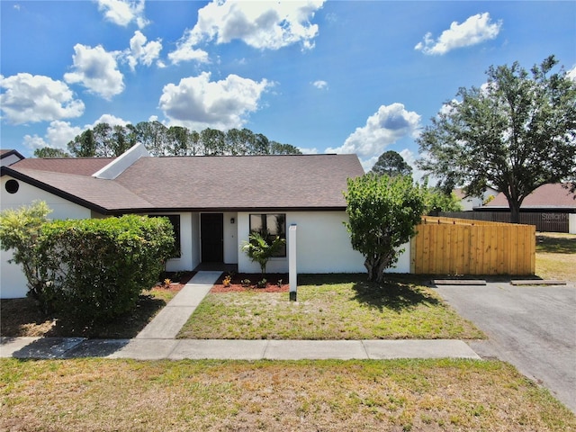 ranch-style home with stucco siding, fence, a shingled roof, and a front lawn