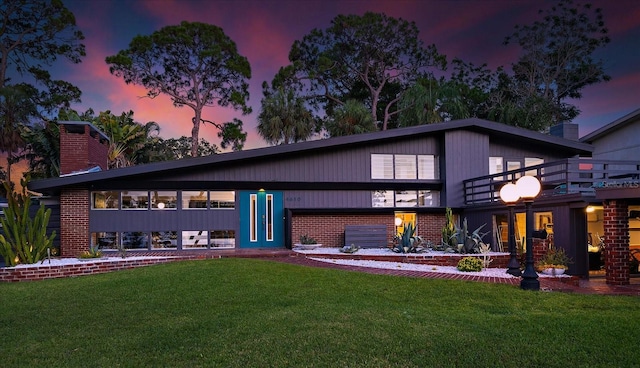 back of property at dusk featuring a lawn, a chimney, and a balcony