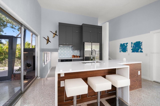 kitchen featuring modern cabinets, a center island with sink, light countertops, freestanding refrigerator, and a breakfast bar