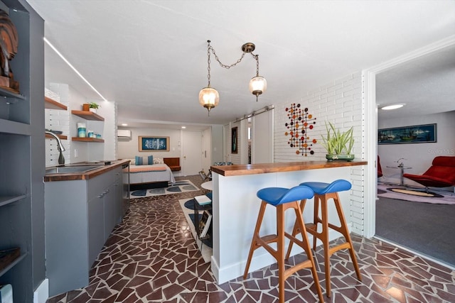 kitchen featuring a kitchen breakfast bar, pendant lighting, stone flooring, a sink, and butcher block countertops