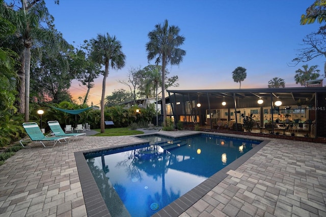 pool at dusk featuring a patio, an outdoor pool, and a sunroom