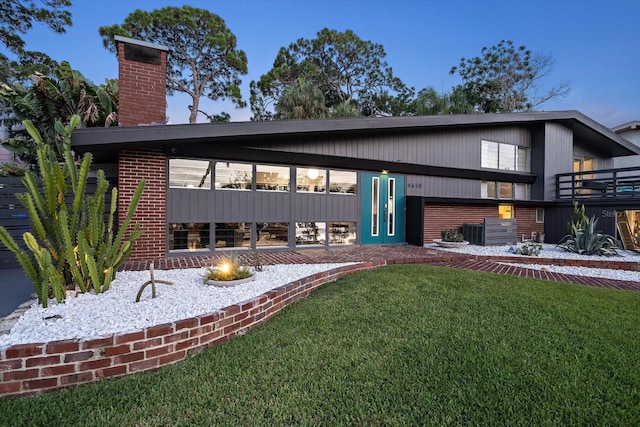 rear view of house featuring a chimney, a patio area, central air condition unit, brick siding, and a yard