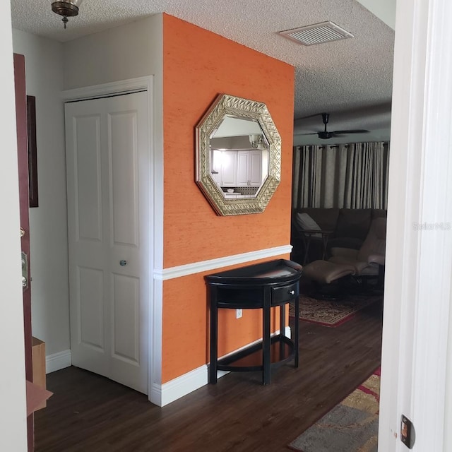 hallway with a textured ceiling, baseboards, visible vents, and wood finished floors