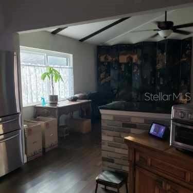 bar with freestanding refrigerator, beamed ceiling, a ceiling fan, and wood finished floors