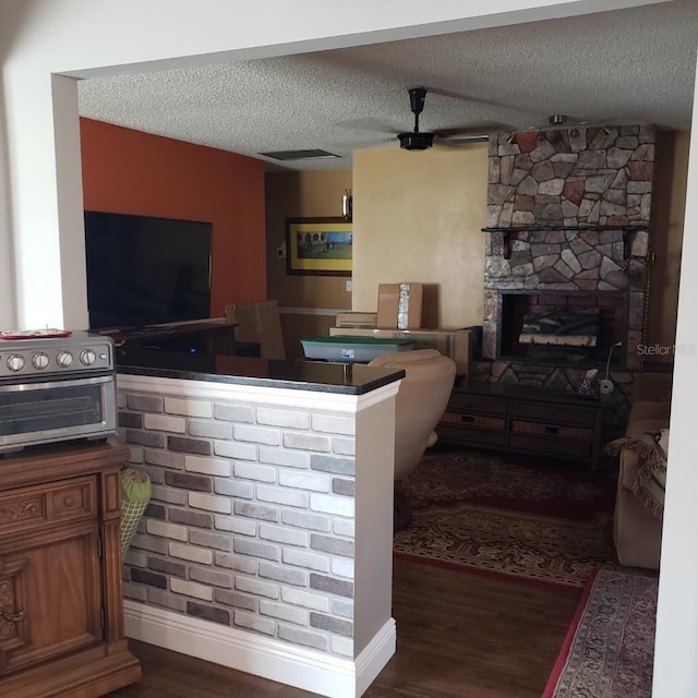 living area featuring wood finished floors, a toaster, a textured ceiling, baseboards, and a stone fireplace