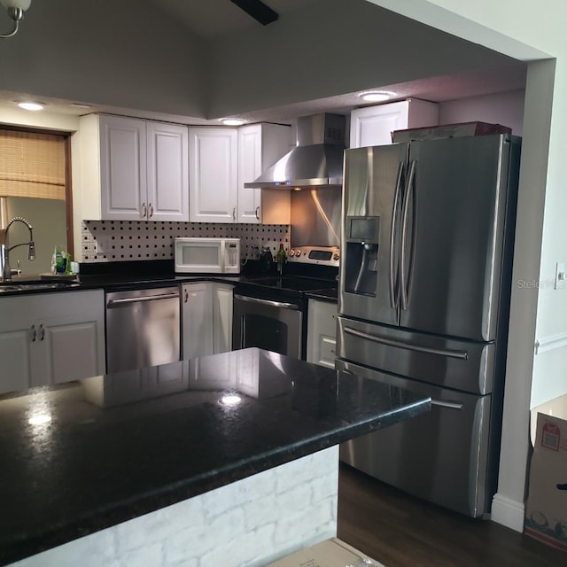 kitchen with a sink, dark countertops, stainless steel appliances, and wall chimney range hood