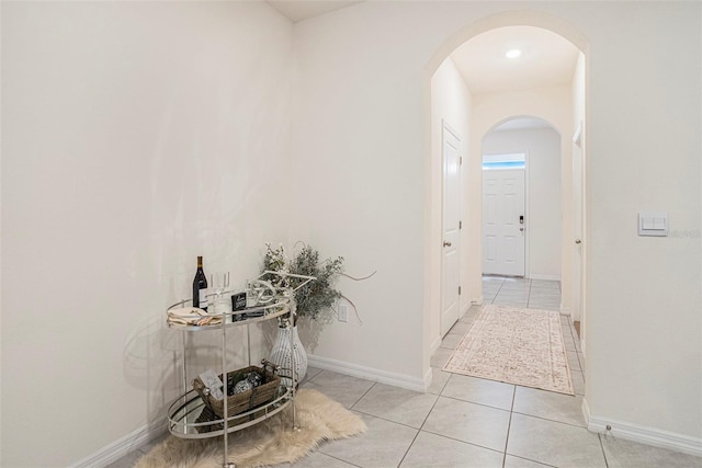 hallway featuring arched walkways, light tile patterned floors, and baseboards
