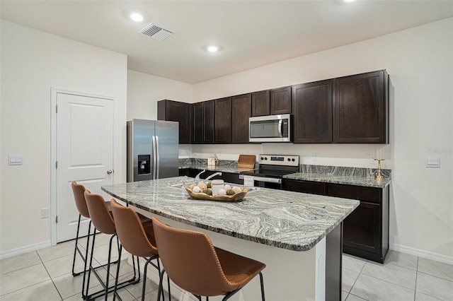 kitchen featuring appliances with stainless steel finishes, light stone counters, a breakfast bar area, a center island with sink, and recessed lighting