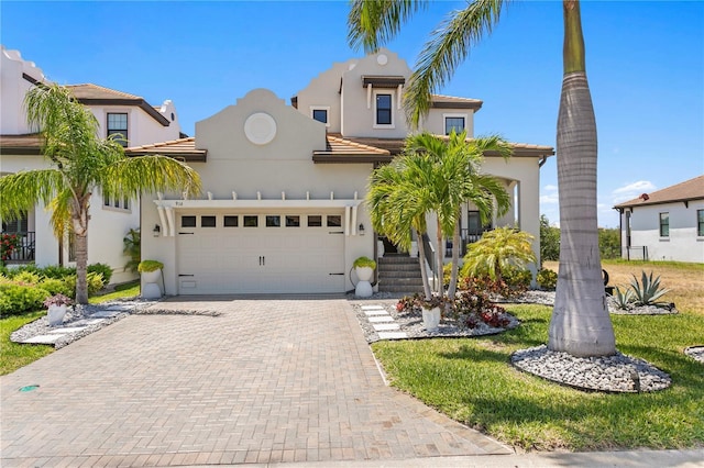 mediterranean / spanish-style house featuring an attached garage, decorative driveway, stucco siding, and a tile roof