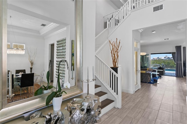 entrance foyer with crown molding, a notable chandelier, stairs, and visible vents