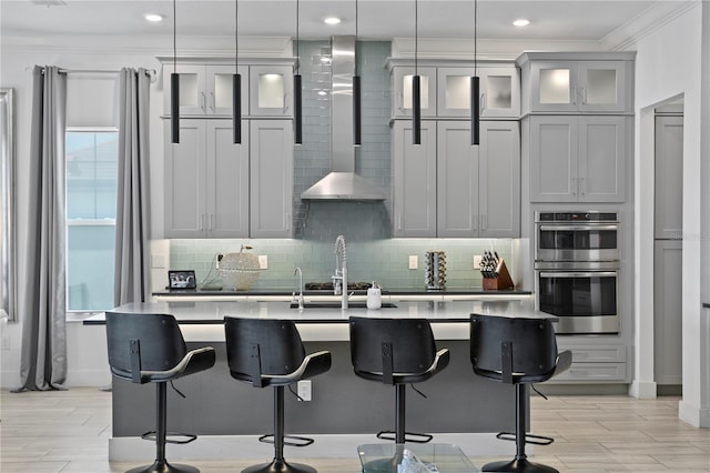 kitchen with crown molding, double oven, a kitchen breakfast bar, an island with sink, and tasteful backsplash