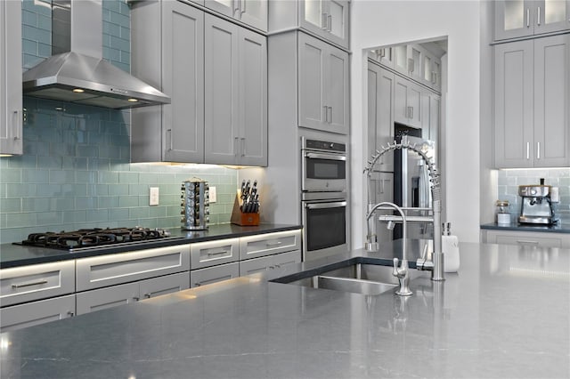 kitchen featuring glass insert cabinets, wall chimney range hood, stainless steel double oven, gas stovetop, and tasteful backsplash