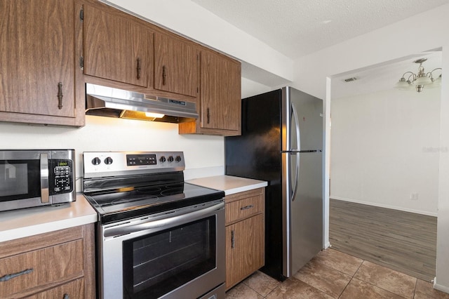 200 Country Club Dr Unit 906, Largo, FL 33771 - kitchen with light countertops, under cabinet range hood, brown cabinets, and stainless steel appliances