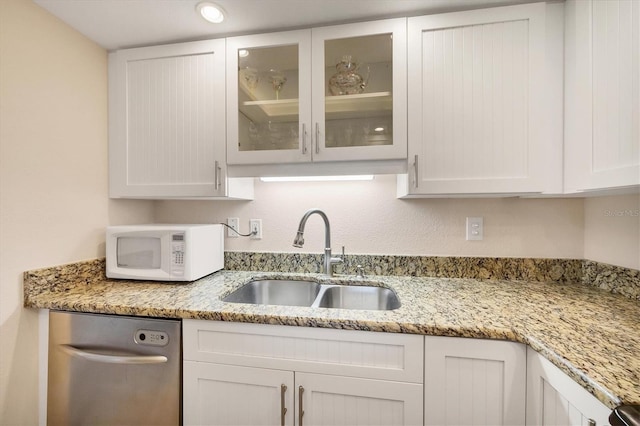 kitchen featuring dishwasher, a sink, white microwave, glass insert cabinets, and white cabinetry