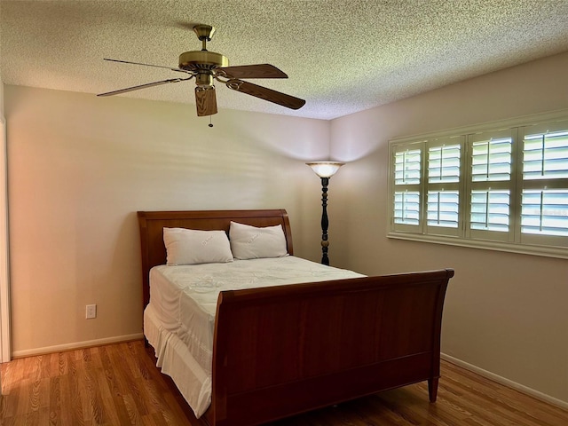 bedroom featuring wood finished floors, a textured ceiling, ceiling fan, and baseboards