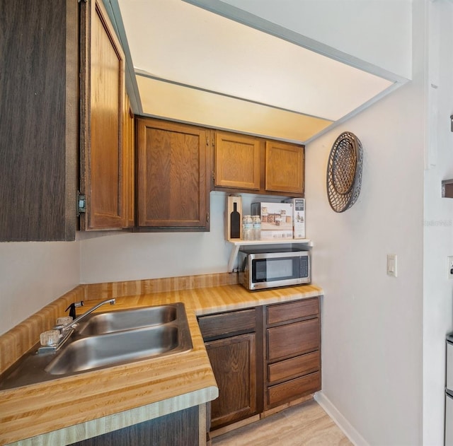 6514 Sunhigh Dr, New Port Richey, FL 34655 - kitchen featuring stainless steel microwave, a sink, butcher block counters, light wood-style floors, and brown cabinets