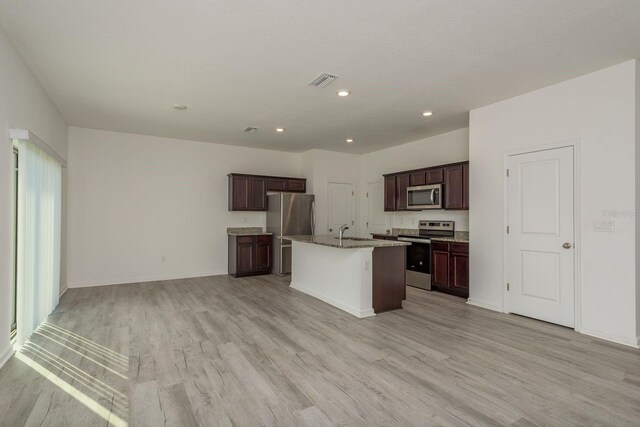 kitchen featuring appliances with stainless steel finishes, light wood-style flooring, a center island with sink, a sink, and open floor plan