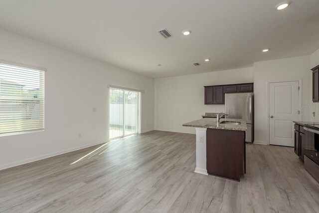 kitchen featuring freestanding refrigerator, light wood finished floors, a kitchen island with sink, light stone countertops, and recessed lighting