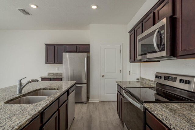 kitchen with appliances with stainless steel finishes, a sink, dark stone counters, light wood-type flooring, and recessed lighting