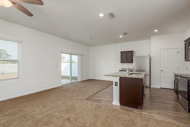 kitchen with appliances with stainless steel finishes, a sink, a center island with sink, a ceiling fan, and dark brown cabinetry