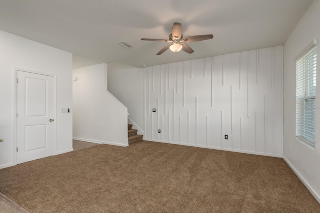 unfurnished living room featuring carpet, a ceiling fan, stairs, and baseboards