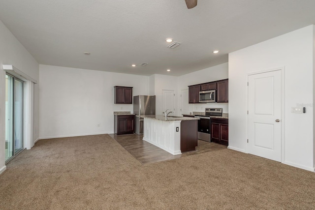 kitchen with appliances with stainless steel finishes, carpet flooring, a sink, a center island with sink, and baseboards