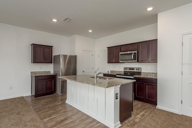 kitchen featuring appliances with stainless steel finishes, a sink, light stone counters, an island with sink, and dark brown cabinetry