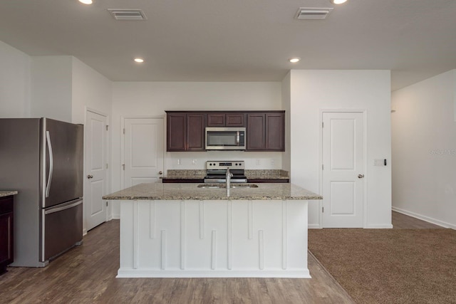 kitchen featuring appliances with stainless steel finishes, light stone counters, dark brown cabinets, a center island with sink, and baseboards