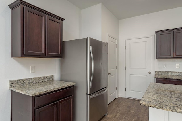 kitchen featuring dark wood-style floors, dark brown cabinets, freestanding refrigerator, and light stone countertops
