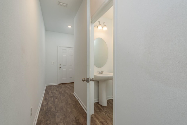 hall featuring wood finished floors, baseboards, and a sink