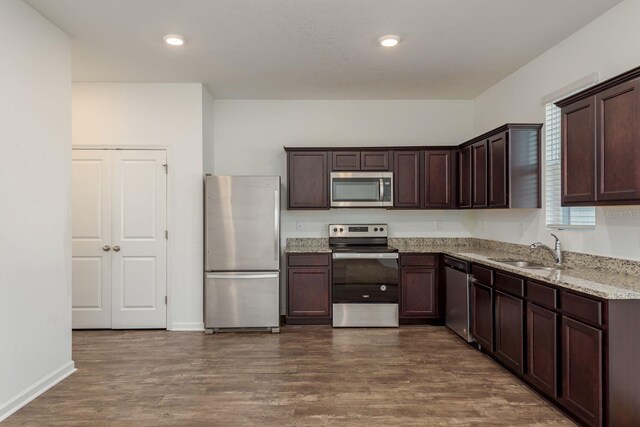 kitchen featuring stainless steel appliances, a sink, dark brown cabinets, dark wood-type flooring, and recessed lighting