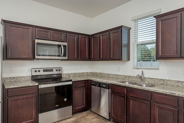 kitchen featuring appliances with stainless steel finishes, a sink, light wood finished floors, dark brown cabinetry, and light stone countertops