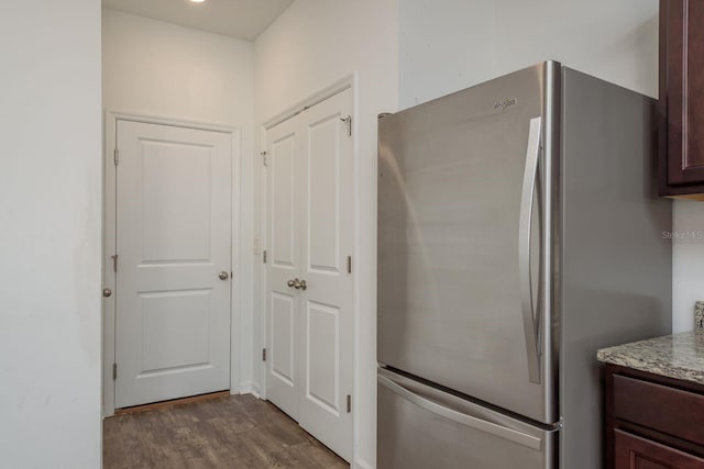 kitchen featuring freestanding refrigerator, dark wood-style floors, dark brown cabinets, and light stone counters