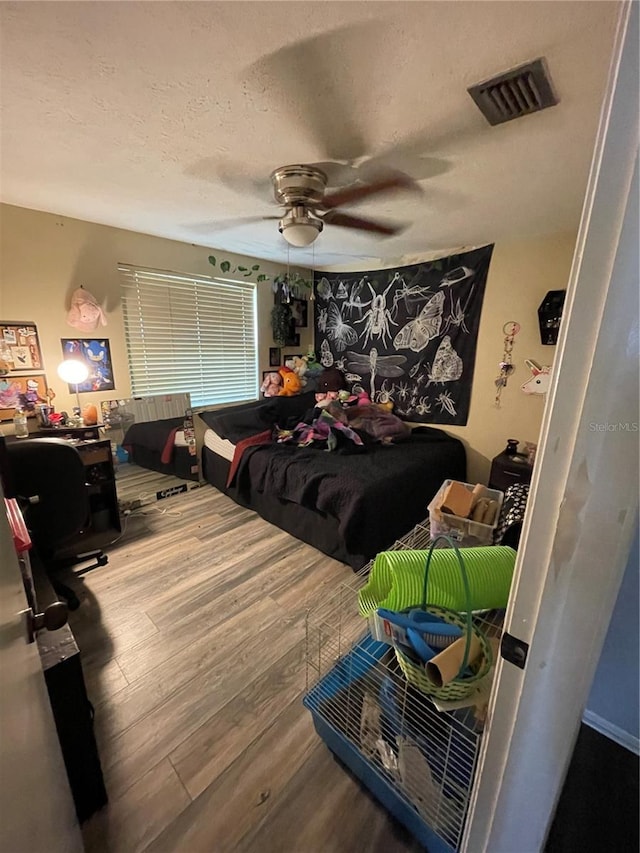 bedroom featuring visible vents, a ceiling fan, a textured ceiling, and wood finished floors