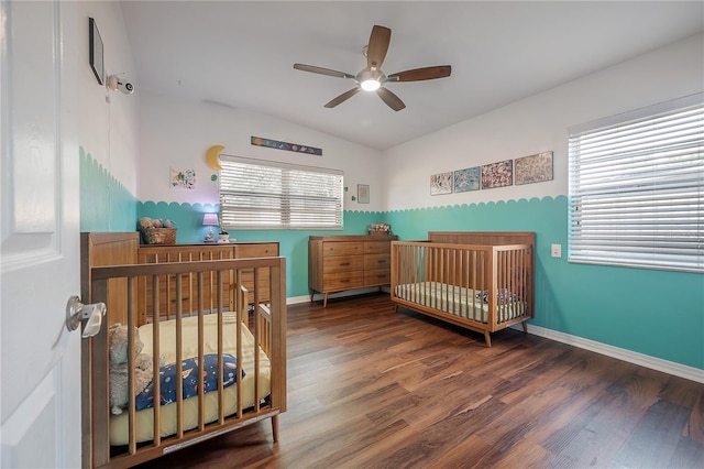bedroom featuring a nursery area, a ceiling fan, baseboards, wood finished floors, and vaulted ceiling