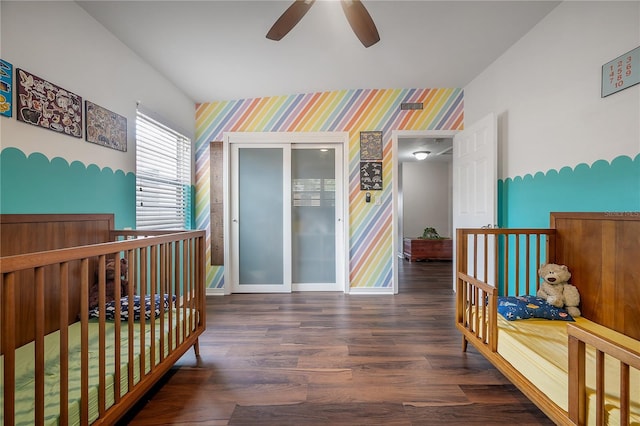 bedroom featuring wood finished floors, an accent wall, baseboards, wallpapered walls, and a crib