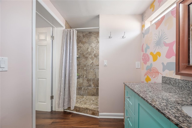 bathroom with vanity, baseboards, wood finished floors, and a tile shower