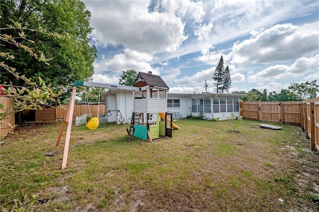 rear view of property featuring a fenced backyard, a lawn, a sunroom, and a playground