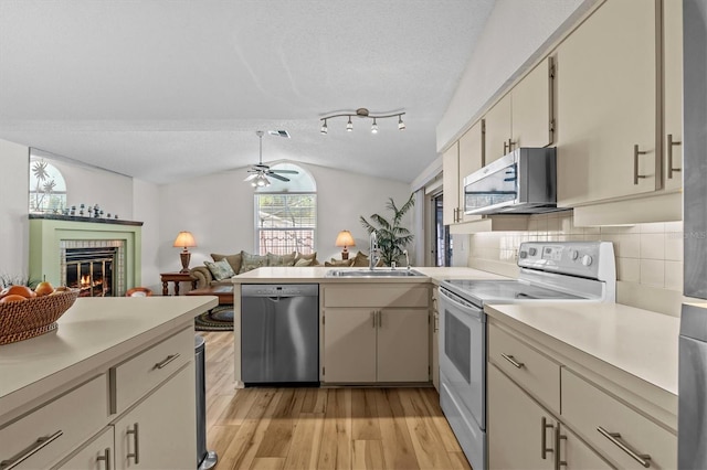 kitchen featuring stainless steel appliances, lofted ceiling, light countertops, light wood-type flooring, and a sink