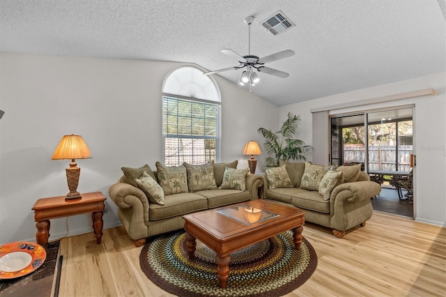 living room with a textured ceiling, plenty of natural light, light wood finished floors, ceiling fan, and vaulted ceiling
