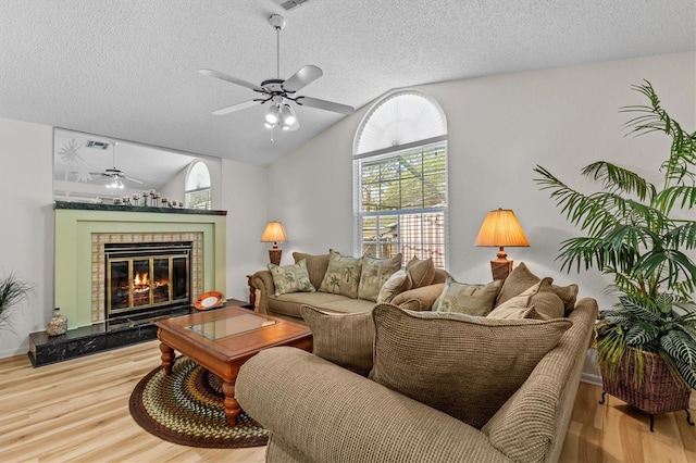living area with ceiling fan, wood finished floors, a textured ceiling, lofted ceiling, and a tiled fireplace
