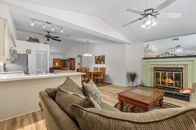 living room featuring vaulted ceiling, a ceiling fan, light wood-type flooring, a glass covered fireplace, and baseboards