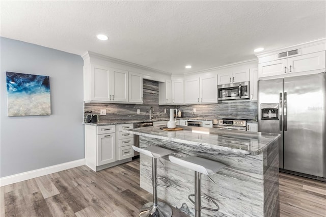 1390 Gulf Blvd Unit Ph-5, Clearwater, FL 33767 - kitchen featuring stainless steel appliances, decorative backsplash, light wood-type flooring, light stone counters, and a kitchen breakfast bar