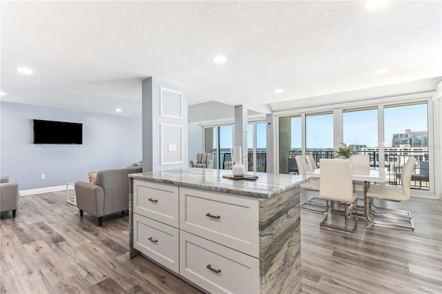 1390 Gulf Blvd Unit Ph-5, Clearwater, FL 33767 - kitchen featuring light wood-style floors, light stone counters, a kitchen island, baseboards, and open floor plan