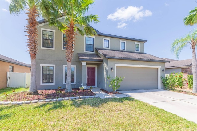 traditional-style home featuring driveway, fence, a front lawn, an attached garage, and stucco siding