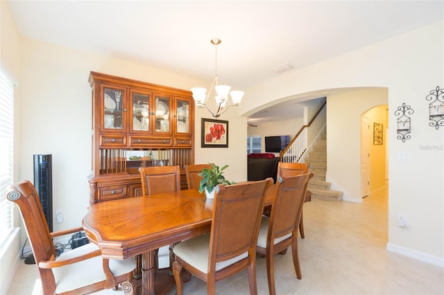 dining room featuring an inviting chandelier, visible vents, stairs, baseboards, and arched walkways