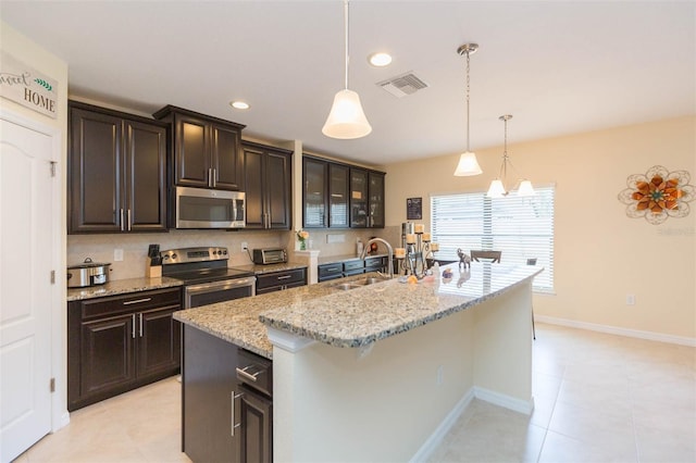 kitchen featuring pendant lighting, an island with sink, light stone counters, a sink, and stainless steel appliances