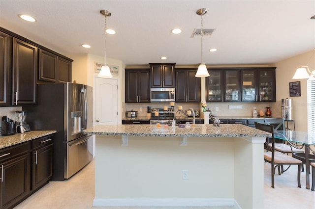 kitchen with a kitchen island with sink, a breakfast bar area, stainless steel appliances, and light stone countertops