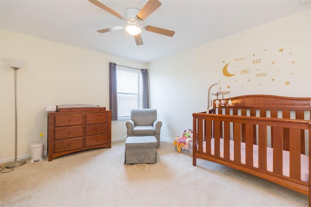 carpeted bedroom featuring a crib, baseboards, and a ceiling fan